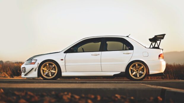 A white Lancer Evo with golden wheels and a rear spoiler parked outdoors at sunset, HD Desktop Wallpaper