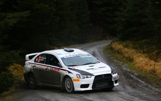 A Lancer Evo racing car drives on a winding forest road covered with gravel, 2K Desktop Wallpaper