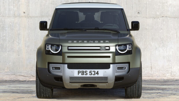 A green Land Rover Defender is parked directly facing a concrete wall, showcasing its grille and headlights, HD Desktop Wallpaper