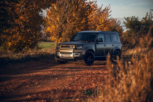 A Land Rover Defender is parked on a dirt road surrounded by autumn trees, 2K Desktop Wallpaper