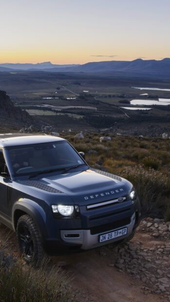 A Land Rover Defender drives through rugged mountain terrain at sunset, 4K Mobile Wallpaper