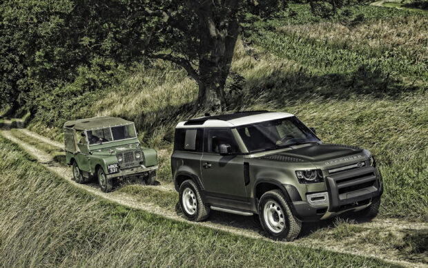 A green Land Rover Defender leads an older model on a rural dirt road surrounded by grass and trees, 2K Desktop Wallpaper