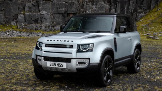 A silver Land Rover Defender is parked on rocky ground near cliffs with green moss, 4K PC Wallpaper