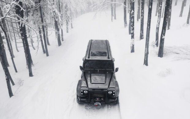 A Land Rover Defender is driving through a snow covered forest path surrounded by tall trees, HD Desktop Wallpaper
