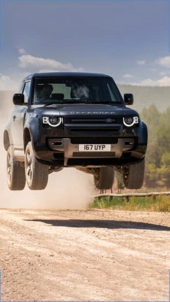 A Land Rover Defender is captured mid air while jumping over a dirt trail in an outdoor setting, 4K Mobile Wallpaper