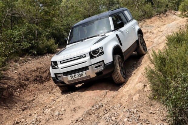A Land Rover Defender navigating rough terrain in a forest setting, HD Desktop Wallpaper