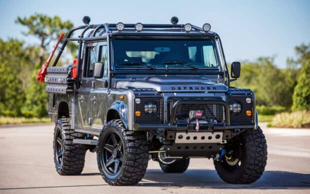 A Land Rover Defender with rugged tires is parked on a road under clear skies, 2K Desktop Wallpaper
