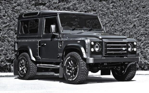 A black Land Rover Defender is parked in front of green bushes with clear details, 2K Desktop Wallpaper