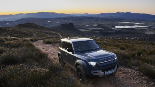 A Land Rover Defender is navigating a rocky dirt path in a mountainous landscape at sunset, HD Desktop Wallpaper