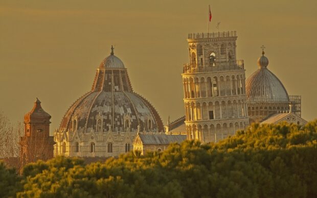 The Tower of Pisa is illuminated by golden light behind green trees, HD Desktop Wallpaper