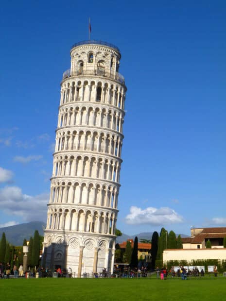 The Tower of Pisa stands leaning on green grass with a bright blue sky, 2K Mobile Wallpaper