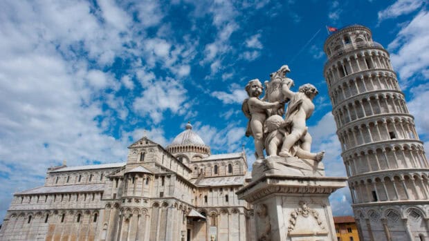 The Leaning Tower of Pisa is standing beside angel sculptures under a bright blue sky with clouds, HD Desktop Wallpaper
