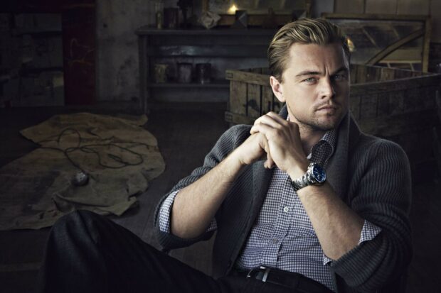 A portrait of Leonardo Dicaprio wearing a watch and sweater sitting thoughtfully in a rustic room, 2K Desktop Wallpaper