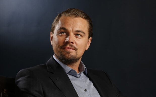 Leonardo Dicaprio Wallpapers shows a thoughtful expression wearing a suit against a dark background, HD Desktop Wallpaper
