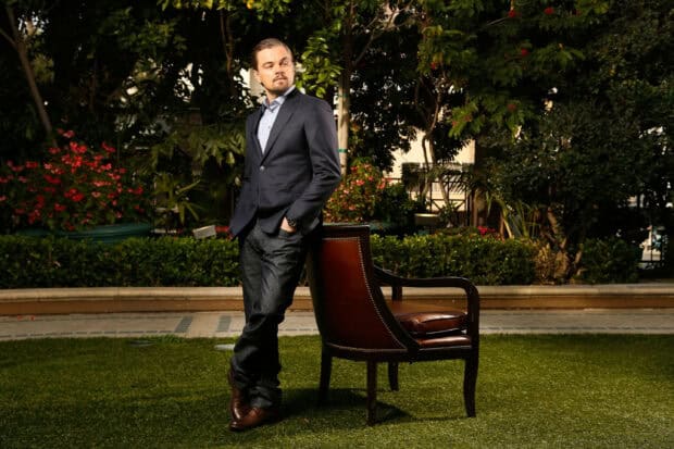 Leonardo Dicaprio is standing beside a chair in a garden with greenery and flowers, 2K Desktop Wallpaper