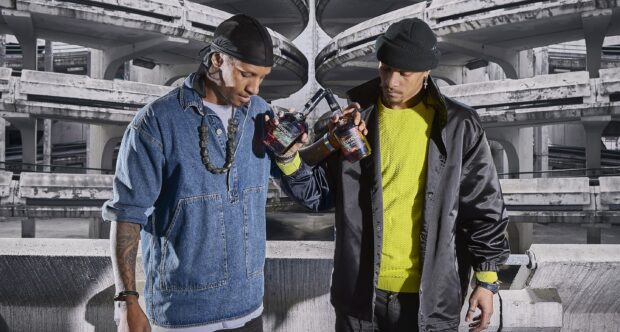 Les Twins holding bottles together in an urban setting with concrete architecture, 2K Desktop Wallpaper