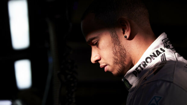Lewis Hamilton is shown in a thoughtful moment wearing his racing suit, HD Desktop Wallpaper
