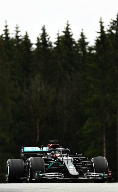 Lewis Hamilton is driving a Formula 1 car on the track surrounded by trees, 2K Phone Wallpaper