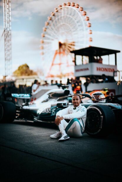 Lewis Hamilton sitting by his Formula 1 car with a Ferris wheel in the background, HD Mobile Wallpaper