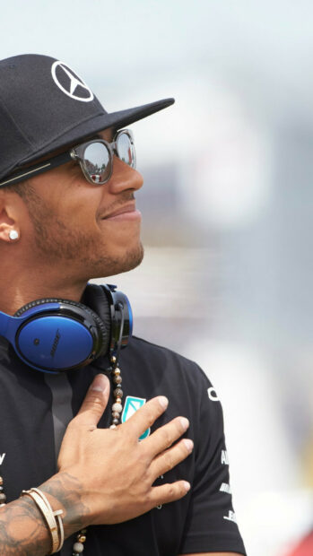 Lewis Hamilton wearing sunglasses and headphones with a hand on his chest, HD Phone Wallpaper