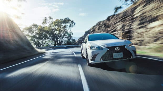 A white Lexus ES driving fast on a winding mountain road with trees and sunlight, HD Desktop Wallpaper
