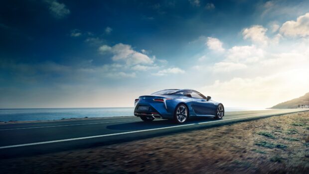 A Lexus LC is driving along a scenic coastal road under a partly cloudy sky, 4K Desktop Wallpaper