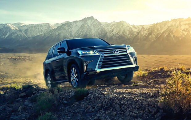 A Lexus LX drives through rocky terrain with mountains in the background during sunset, HD Desktop Wallpaper