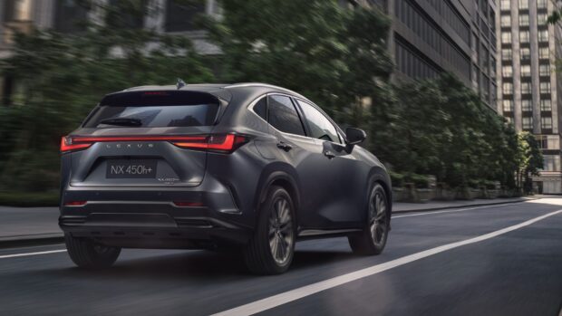 A Lexus NX 450h Plus is driving on a city street surrounded by buildings, HD Desktop Wallpaper