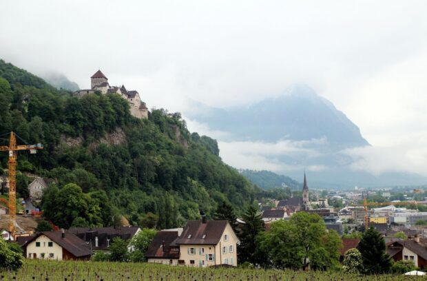 A scenic view of a village with a castle on a hill and mountains in the background, HD Desktop Wallpaper