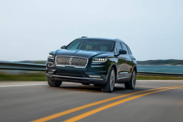 A Lincoln Car is cruising smoothly on a coastal highway with water and hills in the background, 2K Desktop Wallpaper