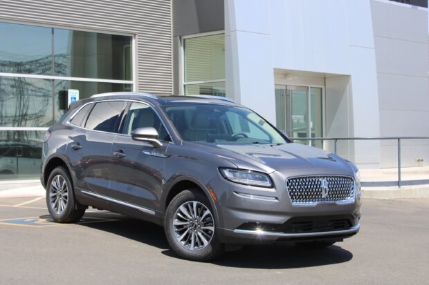 A metallic Lincoln Nautilus is parked outside a modern building under sunlight, 2K Desktop Wallpaper