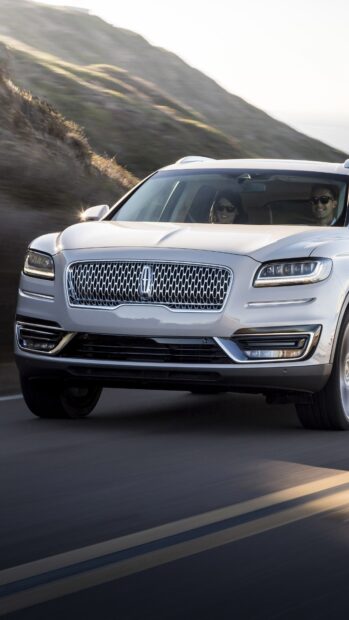 A silver Lincoln car is driving along a winding mountain road with two passengers inside, 4K Phone Wallpaper