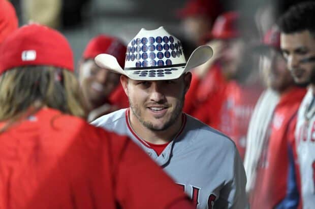 A Los Angeles Angels player wearing a hat covered in team logos is smiling during a game, HD Desktop Wallpaper