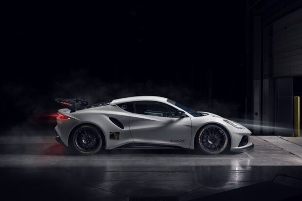 A white Lotus Emira GT2 is parked in a dark garage with lights highlighting its sleek design, 2K Desktop Wallpaper