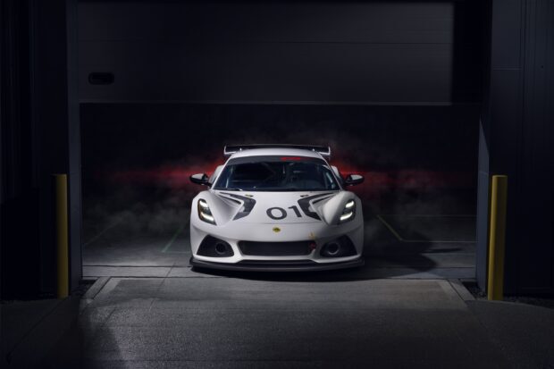 A white Lotus Emira sports car is parked in a dark garage with red smoke behind it, 2K Desktop Wallpaper