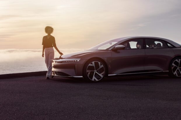 A woman stands next to a Lucid Motors car at sunset near the ocean, 2K Desktop Wallpaper