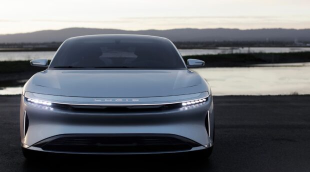 A sleek silver Lucid Motors car is parked near a water body at dusk, 2K Desktop Wallpaper