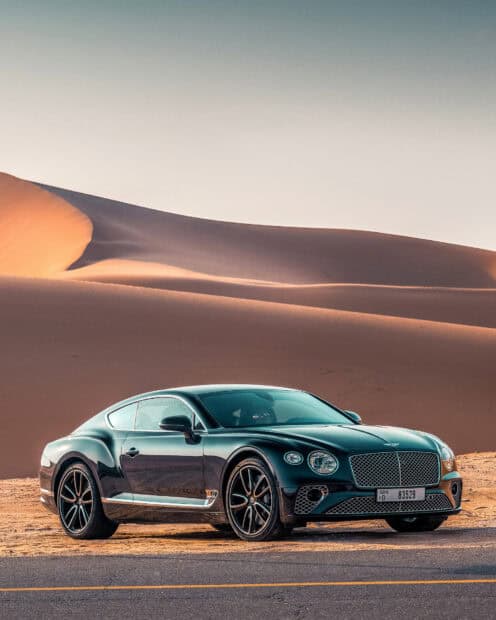 A sleek Bentley Continental GT is parked by smooth desert dunes during sunset, HD Desktop Wallpaper