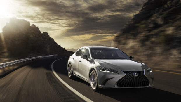 A silver Lexus Es drives smoothly along a winding mountain road under a dramatic sunset sky, 4K Desktop Wallpaper