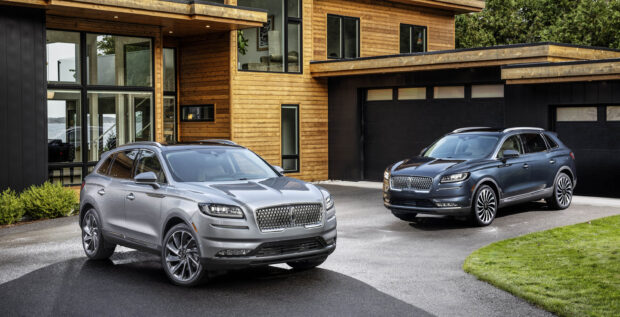 Two Lincoln Nautilus vehicles are parked outside a contemporary home surrounded by greenery, 2K Desktop Wallpaper
