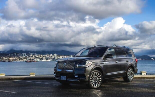 A Lincoln car is parked near the water with a city skyline and cloudy sky in the background, HD Desktop Wallpaper