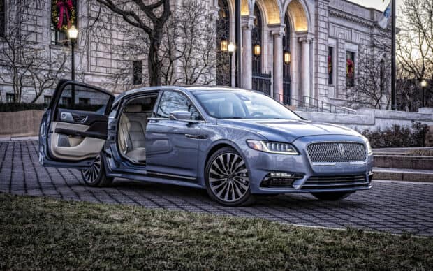 A luxury Lincoln car with an open door is parked on a cobblestone street near a historic building, 2K Desktop Wallpaper
