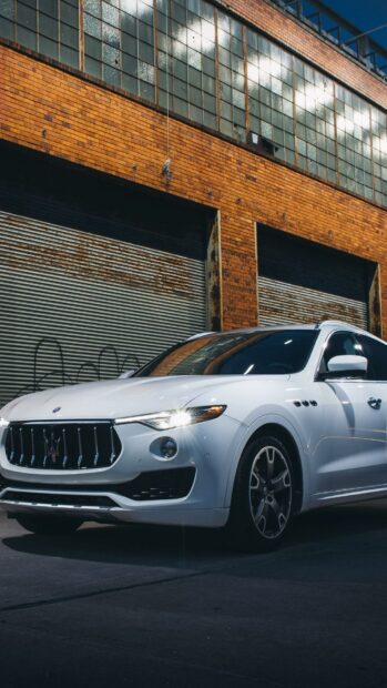 A white Maserati Levante is parked in front of an industrial building with brick walls and large windows, HD Phone Wallpaper