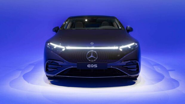 The Mercedes Benz EQS features a sleek front design illuminated by distinctive LED lights against a blue backdrop, HD Desktop Wallpaper