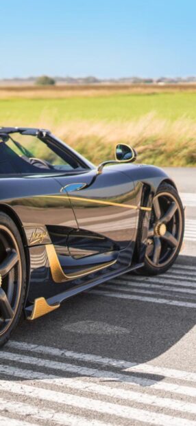 A black Koenigsegg sports car with golden accents parked on the road near a field, 2K Mobile Wallpaper