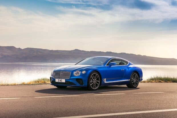 A luxury blue Bentley Continental GT stands on a quiet road with a mountain lake in the background, 2K Desktop Wallpaper