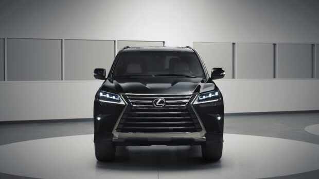 A black Lexus LX SUV is shown from the front with headlights on inside a modern showroom, 4K Desktop Wallpaper