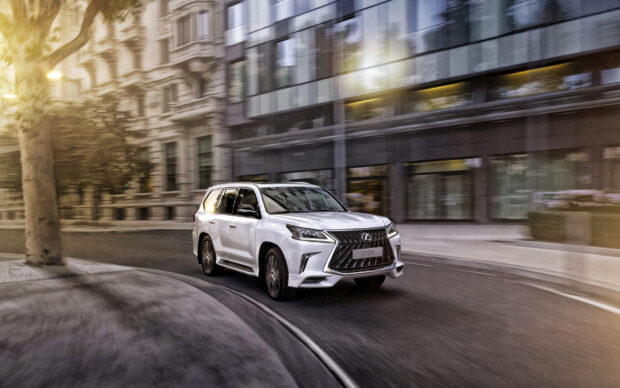 A white Lexus LX is turning a city corner with motion blur capturing its speed, 2K Desktop Wallpaper