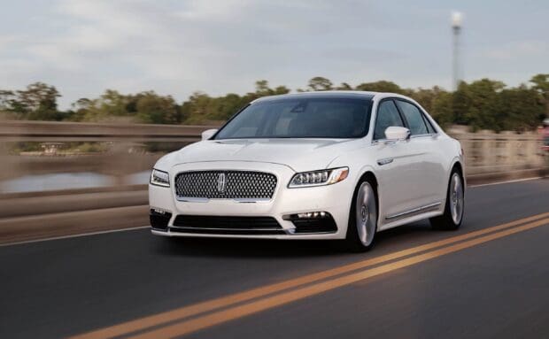 A white Lincoln car is driving smoothly on a highway near a bridge and trees, 2K Desktop Wallpaper