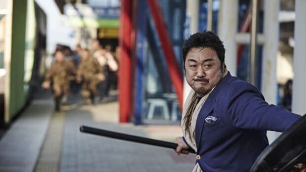 Ma Dong Seok holds a weapon in an intense action scene at a busy station, HD Desktop Wallpaper